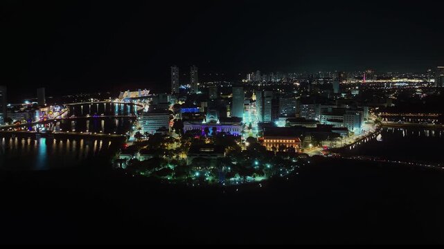 Aerial night view of the city of Recife, Pernambuco, Brazil, highlighting the illuminated urban center and the Pal&aacute;cio do Campo das Princesas along the river. 