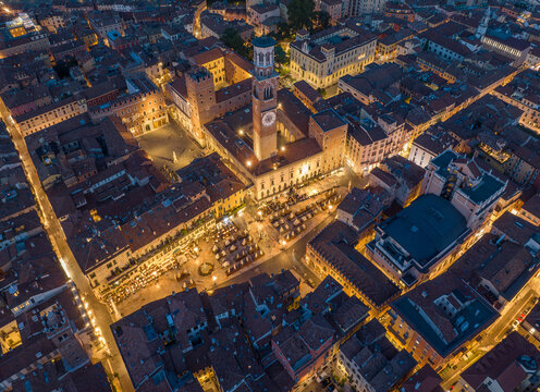 Night view of Piazza delle Erbe with the Torre dei Lamberti illuminated above the square. Historic buildings, warm lights, and lively atmosphere define Verona most iconic public space after dark