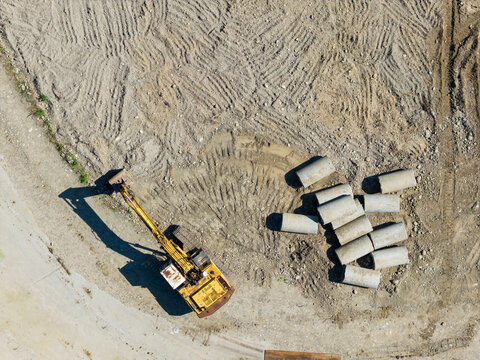 Yellow Excavator and Concrete Pipes at Sandy Construction Site