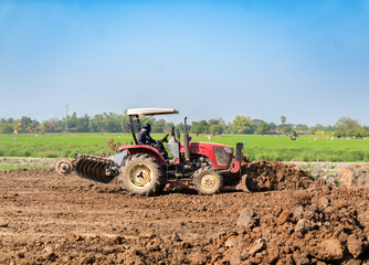 Tractor with front dozer blade and disc harrow working on land preparation and soil leveling.