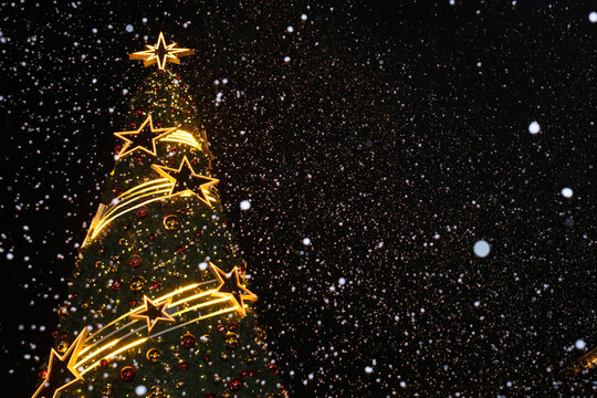 Snow falls around a brightly lit Christmas tree during winter night