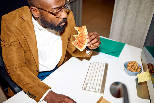 Man bites a pizza slice in the office