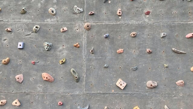 An artificial rock climbing wall with various pastel colored holds on a gray concrete surface, featuring a rough texture, as well as the concept of sports, training, and recreational activities.