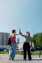 Obraz premium Two women greet each other with a high five in a park on a sunny day while wearing casual clothes and enjoying their time outside