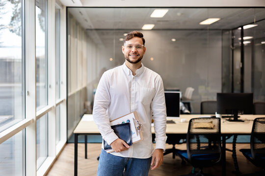 Smiling young businessman holding documents in modern office