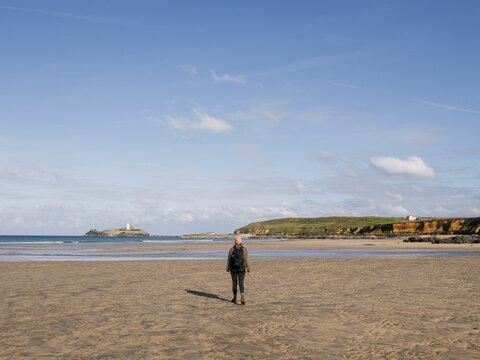 A traveler walks along a sandy beach toward a lighthouse on Godr
