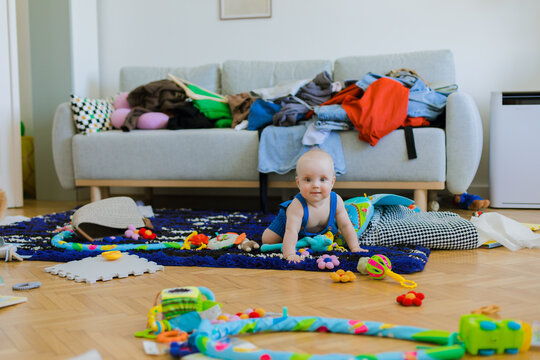 A big mess in a living room, a child is lying on carpet