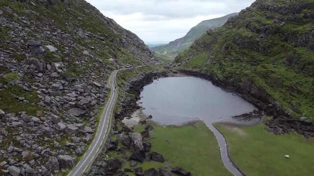 Aerial of a winding road through a rocky valley with a lake.