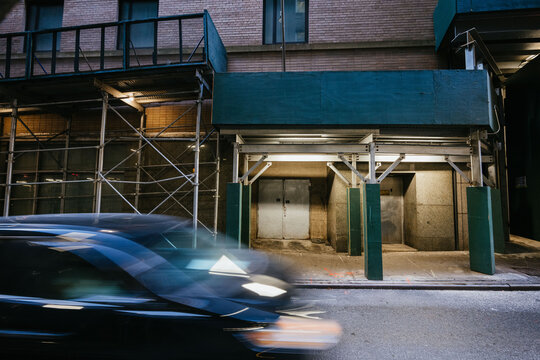Blurred car passes building scaffolding and entrance