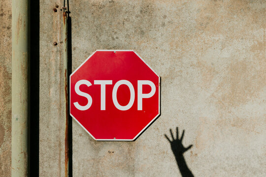 Shadow hand and stop sign against concrete wall