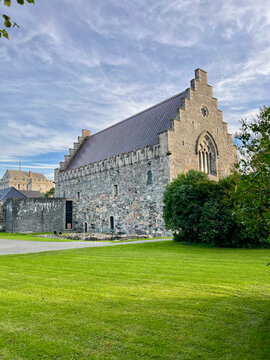Historic stone architecture of Bergenhus Fortress in Bergen, Norway, captured on a bright day with lush green grass and dramatic clouds.