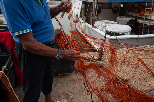 Fisherman Repairing Fishing Net on Small Boat