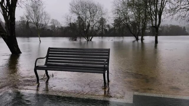 An empty park bench stands abandoned during the river flood.