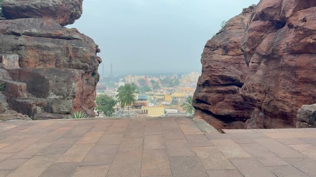 A panoramic dense view of Badami city seen from the caves, nestled between two towering red sandstone hills, capturing the city&rsquo;s layout and the natural beauty surrounding the historic rock-cut temple
