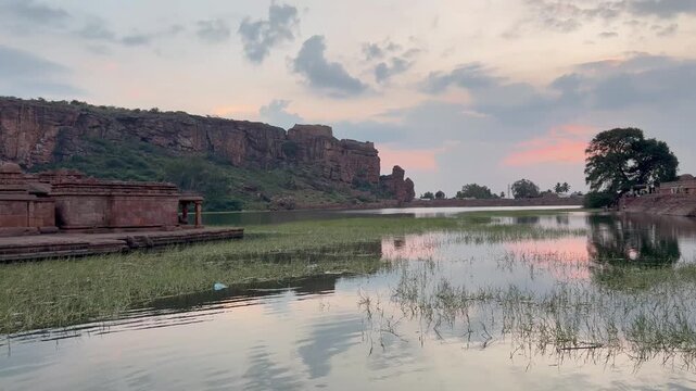 A beautiful view of Bhoothanatha Temple beside the sacred Agastya Lake, set against striking red sandstone hills