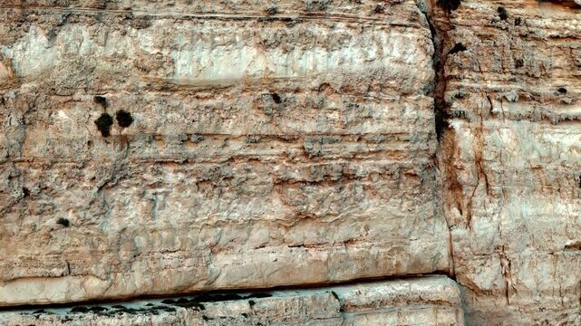 Golden sunlight illuminates the ancient limestone textures of a weathered cliff face in Malta during a warm summer afternoon captured from a wide eye-level angle showcasing rugged organic details