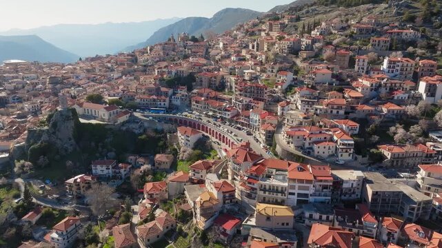 Sweeping aerial medium revealing layered rooftops and winding streets across Parnassus hillside town Arachova, Greece