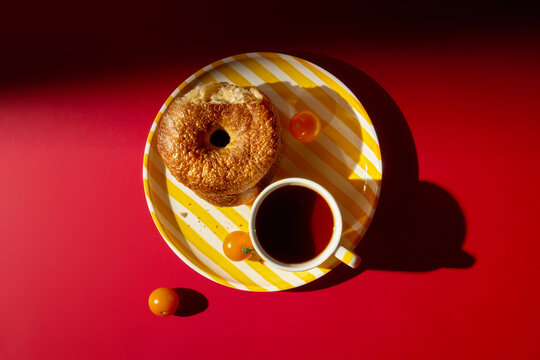 Breakfast With a Bagel and a Black Tea on a Striped Plate on Red Table