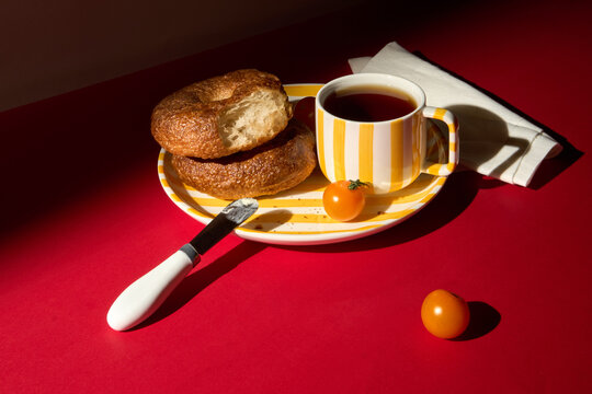 Breakfast With Bagels and Black Tea on a Striped Plate on Red Table