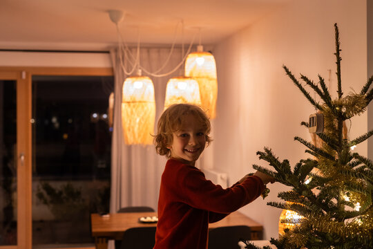 child decorating Christmas tree at home, portrait looking at camera