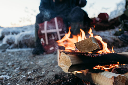 Person warming by campfire on frosty lakeshore morning