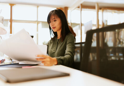 Focused asian woman reviewing documents at her desk