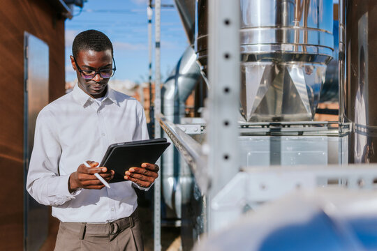 Engineer inspecting HVAC equipment with tablet outdoors