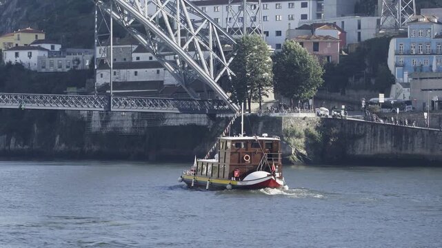 Traditional Rabelo boat sailing on the Douro river near the bridge.