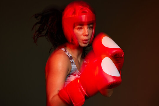 A woman stands in a boxing stance wearing red gloves and headgea