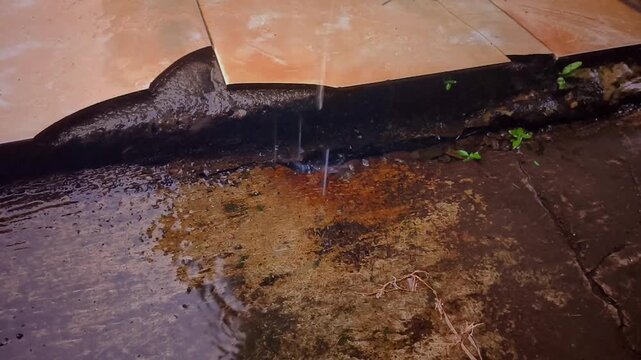 Water leaking from roof onto dirty floor tiles.