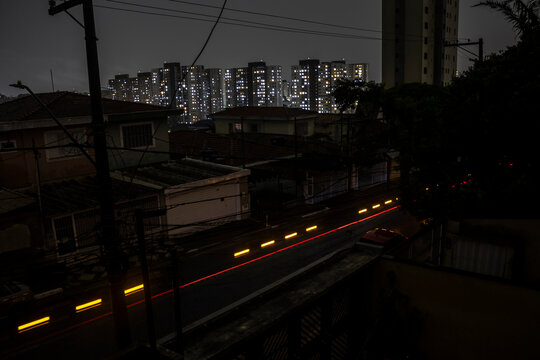 A street in Sao Paulo south side darkens during a blackout. Vulnerable overhead power lines contrast with brightly lit skyscrapers, highlighting the city's deep social and infrastructural divide.