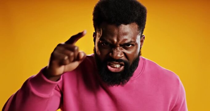 A man in a pink sweater passionately pointing at the camera against a vibrant yellow background