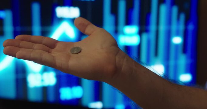 Conceptual stock footage showing a hand holding a small coin in front of a digital market chart, captured in slow motion to symbolize small gains, modest profits, cautious investing, and incremental f