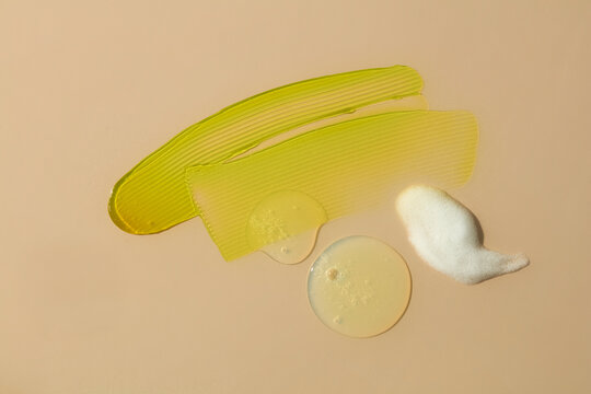 Yellow cosmetic oil with white cream smear on beige background. Abstract skincare texture showing contrast between oil and cream formulations