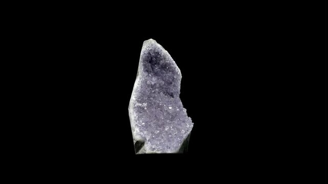 Studio shot of a sparkling mineral geode slowly rotating on black background with dramatic light.