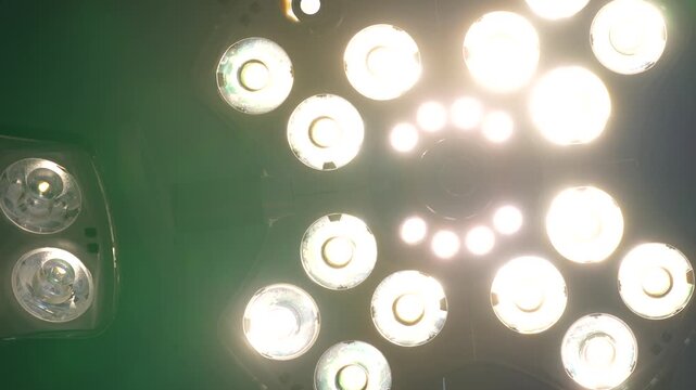 Close-up footage of a hand repositioning an overhead surgical light toward the viewer in a dark operating room with ambient lights turned off, highlighting focused illumination and contrast.