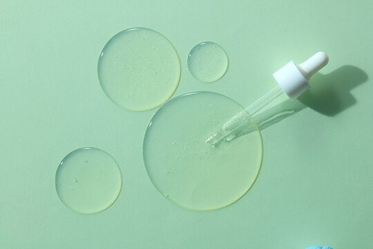 Serum bubbles with glass dropper on green background. Clean skincare texture illustrating cosmetic liquid formulation and laboratory beauty concept