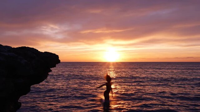Woman jumping off cliff into ocean at sunset
