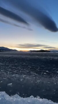 A high-quality vertical shot capturing the mesmerizing blue ice surge at Sayram Lake, Xinjiang, China. The crystal-clear ice blocks move dynamically with the water against a backdrop of snow-capped mo