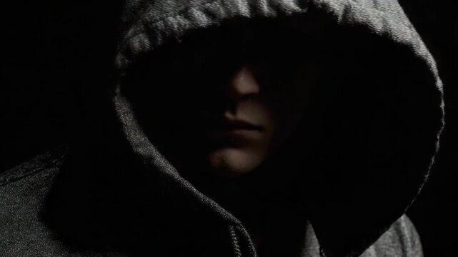 Mystery Within Shadows: A person shrouded in a hooded sweatshirt, their face partially obscured by darkness, creates a sense of enigma and introspection. This image evokes feelings of intrigue.