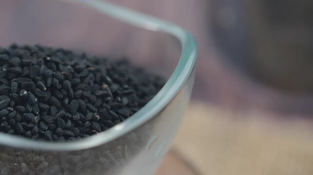 Black cumin seeds in a glass bowl on a wooden surface