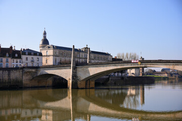 Obraz premium Panoramic view of traditional stone bridge and historic buildings reflecting in river under clear blue sky. Chalon sur Saone