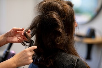 Rear view stylist teasing hair volume, hands backlighting frizz and texture visible, fingers shaping sections, finishing product pending, focused salon prep mood