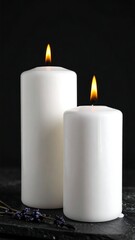 Two white lit candles and lavender on a dark, textured surface