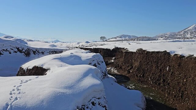 A deep winter ravine with flowing water cuts through a snowy landscape, exposing dark earth beneath the snow under clear blue skies.
📍Marivan, Kurdistan 