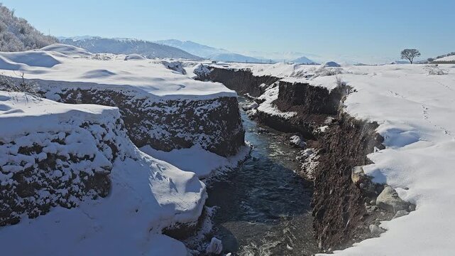 A deep winter ravine with flowing water cuts through a snowy landscape, exposing dark earth beneath the snow under clear blue skies.
📍Marivan, Kurdistan 