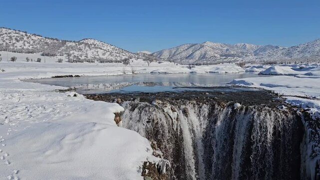 A winter waterfall drops into a snowy gorge, surrounded by frozen terrain and distant mountains under a clear blue sky.
📍Marivan, Kurdistan 