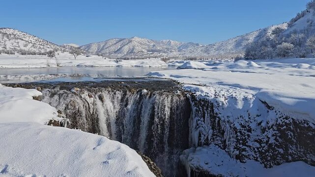 A winter waterfall drops into a snowy gorge, surrounded by frozen terrain and distant mountains under a clear blue sky.
📍Marivan, Kurdistan 