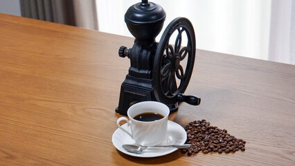 アンティークな雰囲気の黒いコーヒーミルといカップに注がれたブラックコーヒー