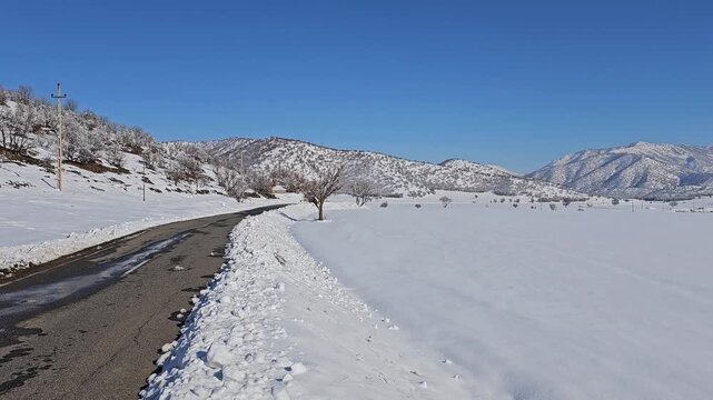 Winter road stretching through a snowy landscape with distant mountains and clear blue sky, capturing the calm beauty and quiet atmosphere of cold-season travel.  
📍Marivan, Kurdistan 